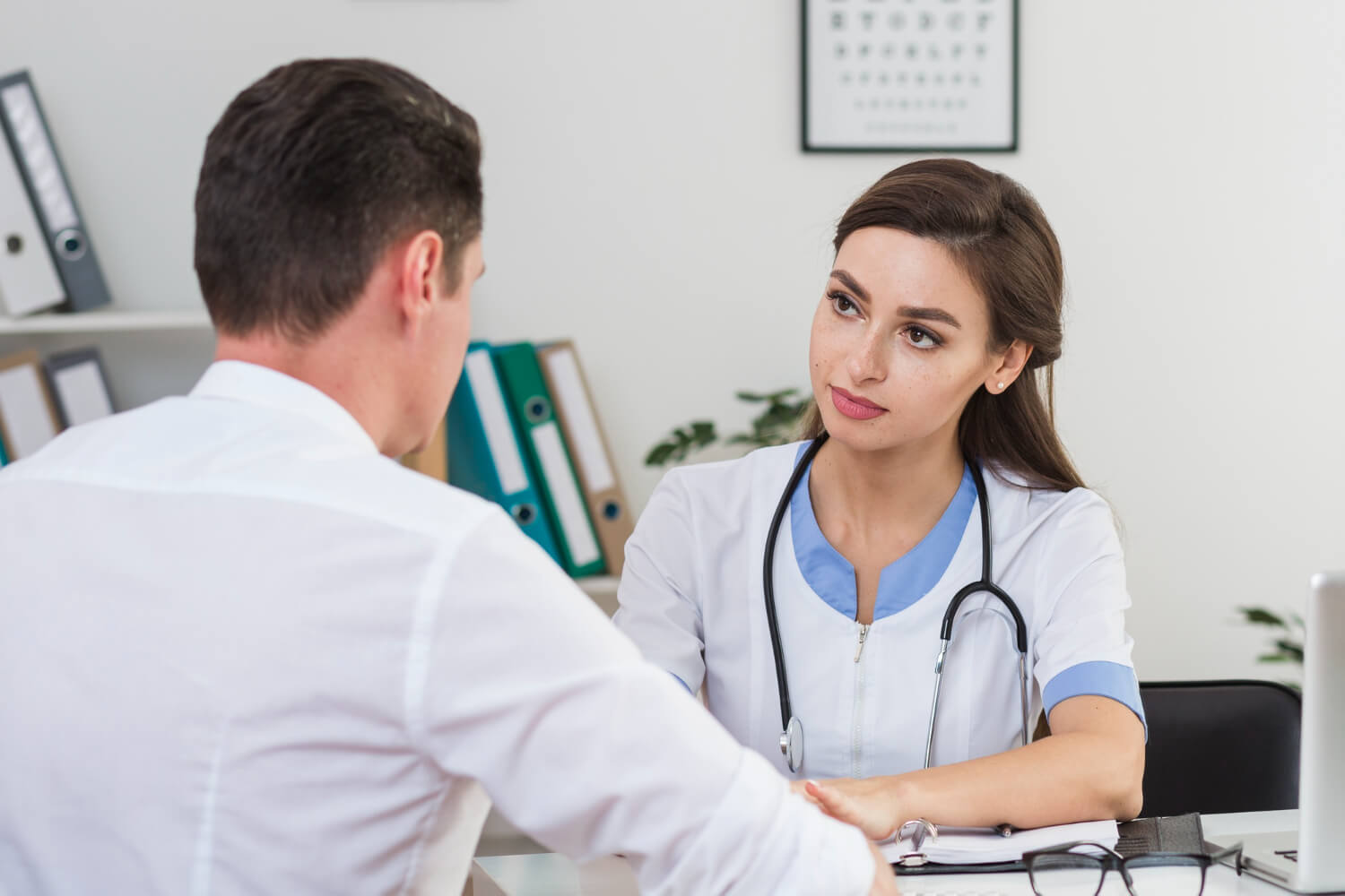 a woman in white coat and stethoscope sitting at a table with a man in a white coat